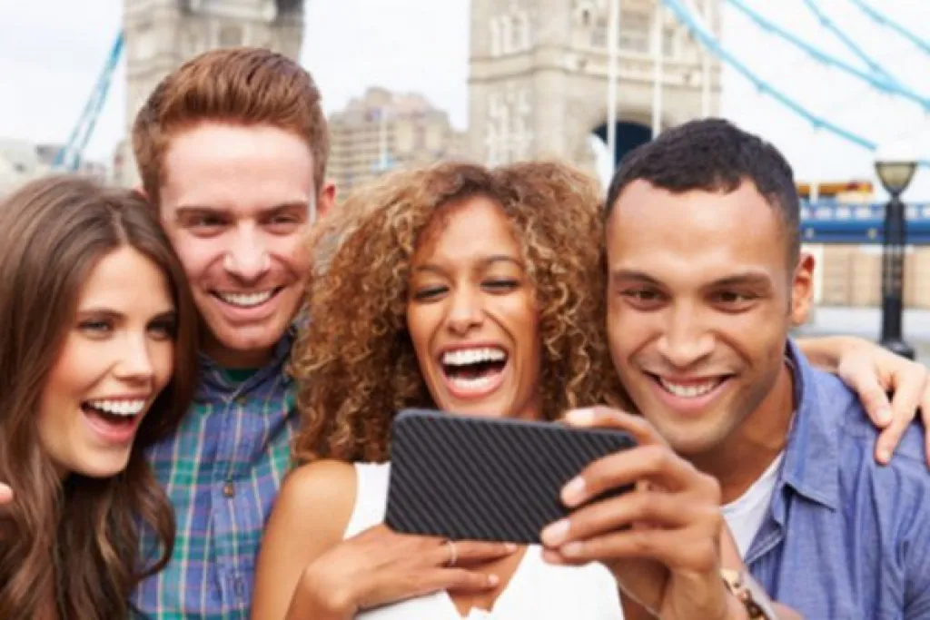 Group of four people are smiling and taking a selfie in front of a bridge.