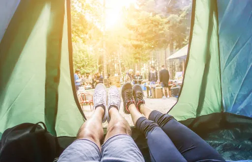 View from inside a tent showing two pairs of feet with a campsite in the background.