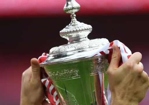 A pair of hands holding a shiny trophy wrapped in a red and white ribbon.