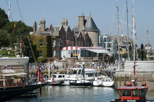 Busy marina with various boats and a historic building in the background under a clear blue sky.