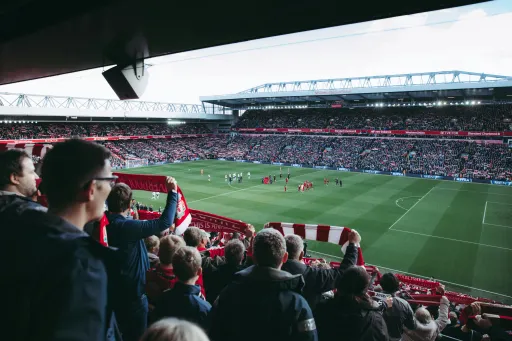 Crowd holds scarves while watching a football match in a stadium filled with spectators.