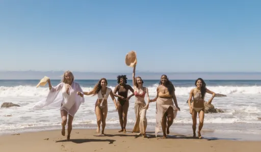Group of people runs along a beach, smiling and enjoying the ocean waves.