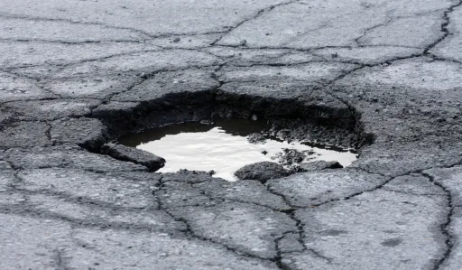 Large pothole filled with water on a cracked asphalt surface.