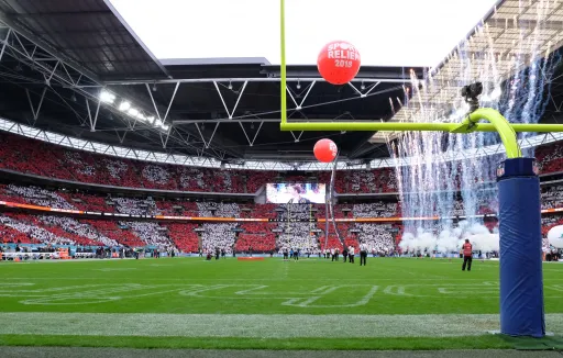 A view of a stadium filled with spectators holding red and white cards, with fireworks and balloons in the foreground.