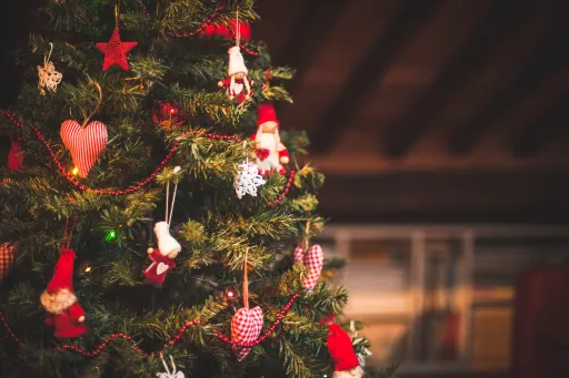A decorated Christmas tree with red and white ornaments, including hearts and small figures, set in a warm indoor space.