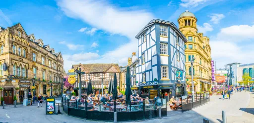 A vibrant street scene featuring historic buildings, outdoor seating, and people enjoying the day under a blue sky.