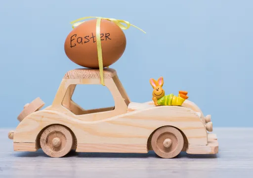 Wooden toy car with an egg labelled Easter on top and a small bunny figurine lying on the side.