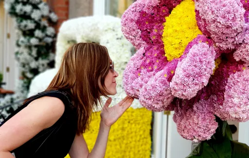Person leans towards a large, colourful flower display, appearing to interact with it.