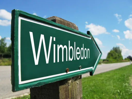 Green signpost pointing right, displaying the word Wimbledon against a blue sky with clouds.