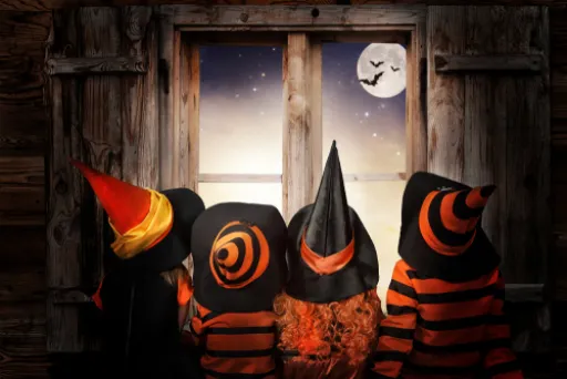 Four figures in witch hats and striped outfits look out of a window at a moonlit night with bats flying.