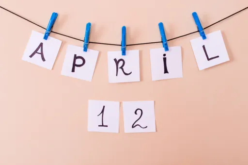 String displays the word APRIL and the number 12 on white cards with blue clips against a peach background.