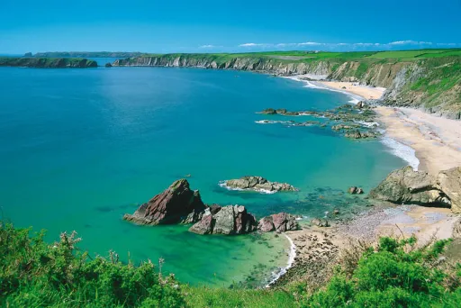 A scenic coastal view featuring turquoise waters, rocky formations, and sandy beaches under a clear blue sky.
