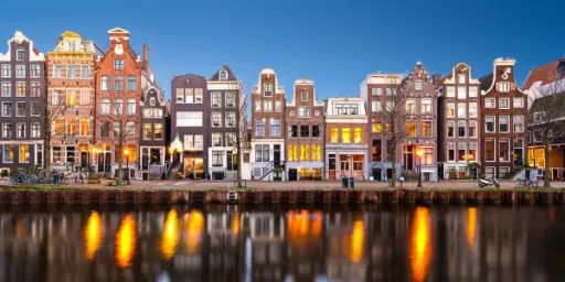 Row of traditional Dutch houses along a canal, reflecting in the water at dusk.