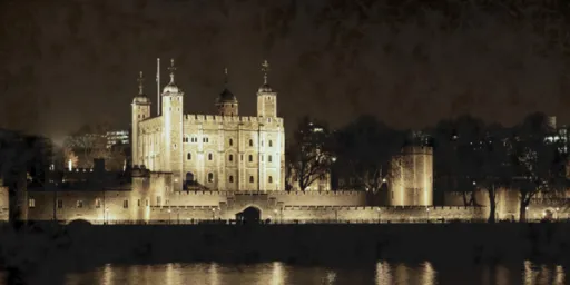 A historic castle illuminated at night, surrounded by a wall and reflected in the water.