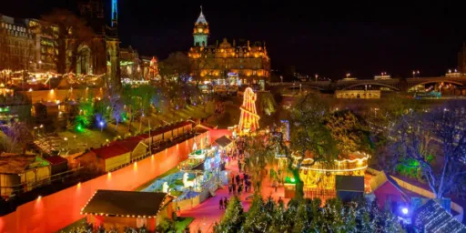 A vibrant night scene of a festive market with lights, stalls, and decorations, set against a city backdrop.