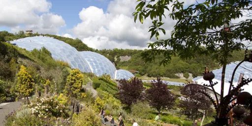 A view of large, transparent domes surrounded by greenery and flowers, with people walking along a path.