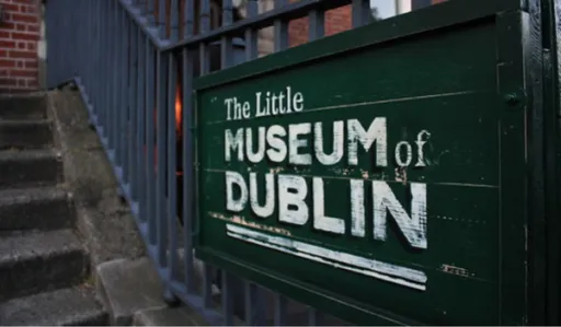 Sign for The Little Museum of Dublin, mounted on a railing near steps. The sign is green with white text.