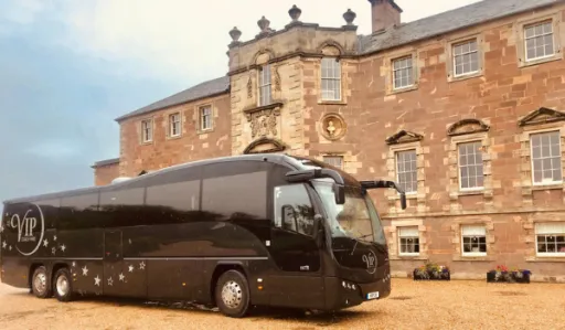Black VIP bus is parked in front of a large stone building with multiple windows.