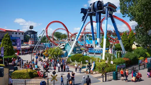Busy amusement park with roller coasters, rides, and people enjoying the day under a blue sky.