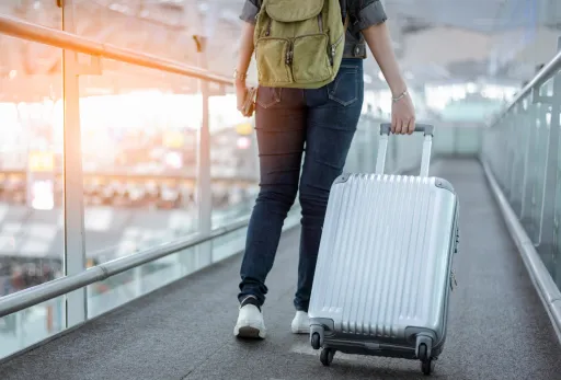 Person walks through an airport terminal while pulling a silver suitcase.