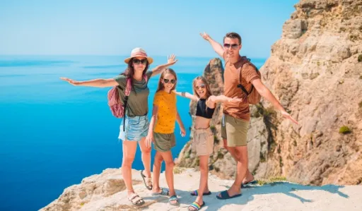 Group of four people stands on a cliff by the sea, with arms outstretched and smiling.