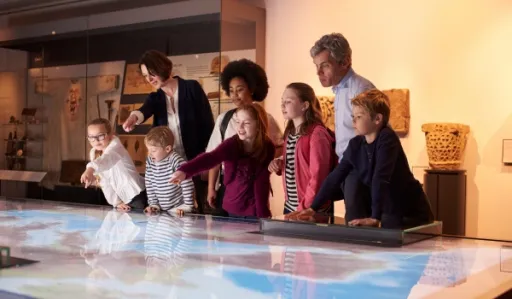 Group of people interact with a digital display in a museum, pointing and observing together.