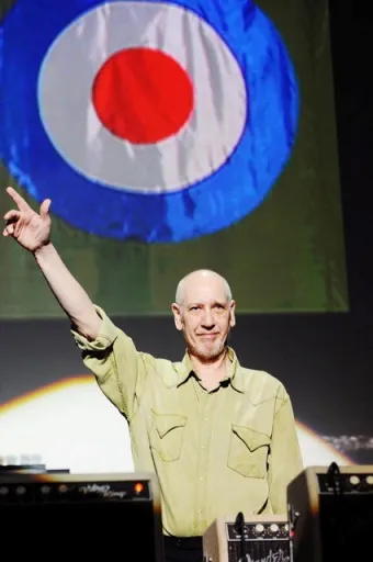A person with a bald head raises one hand while smiling, with a large circular graphic in the background.