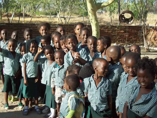 A group of children in matching checkered shirts and skirts, smiling and posing together outdoors.