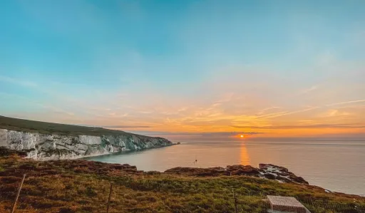Scenic view of cliffs by the sea at sunset, with a calm ocean and a colourful sky.