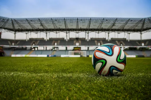 Football rests on the grass in an empty stadium with seating in the background.