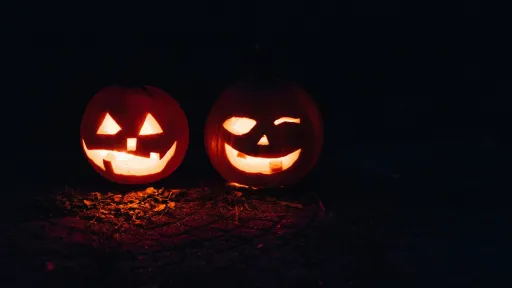 Two carved pumpkins with glowing faces sit on the ground in a dark setting.