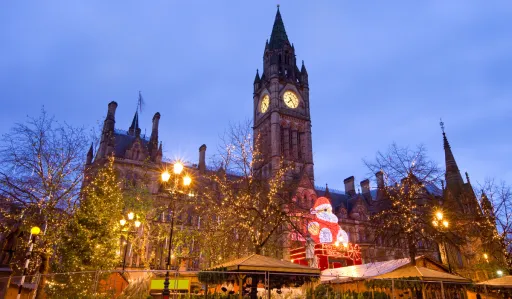 Historic building with a clock tower, decorated with lights and a festive display, under a twilight sky.