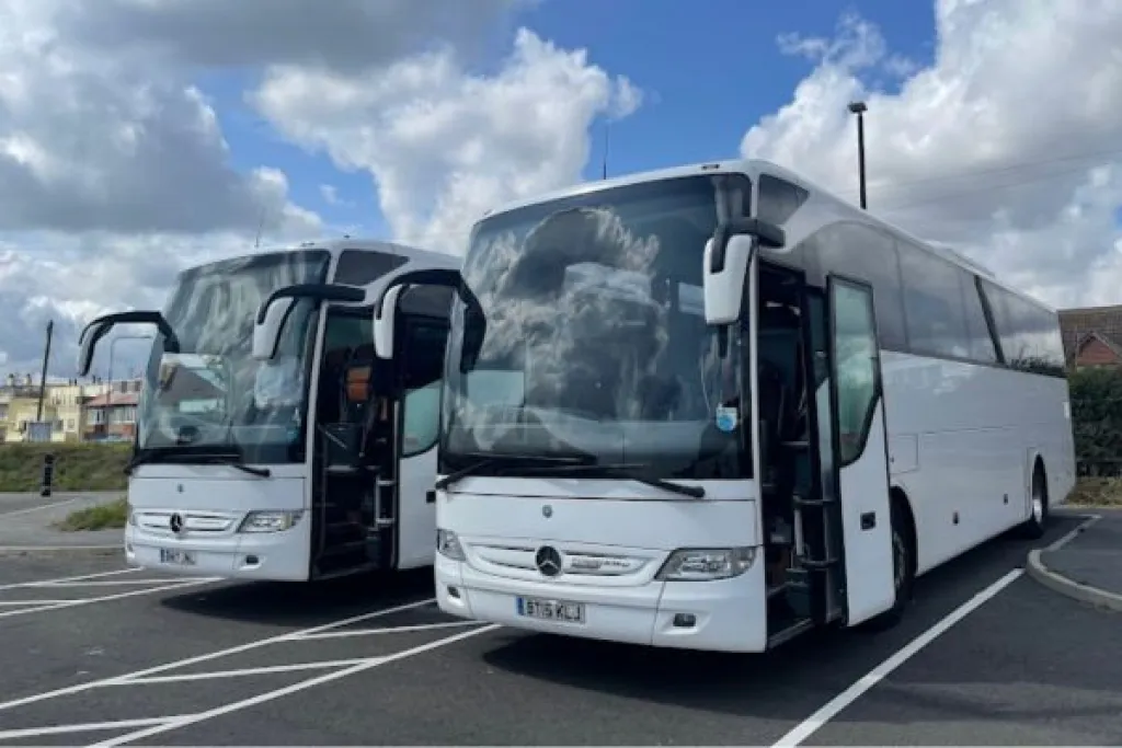 Two white buses parked in a lot under a cloudy sky.