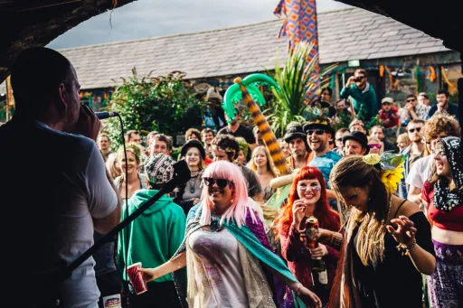 A crowd enjoying a performance outdoors, with a person singing on stage and colourful decorations in the background.