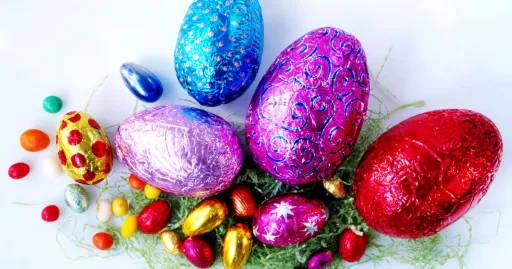 Colourful Easter eggs in various sizes and designs, surrounded by small chocolate eggs and green grass-like material.