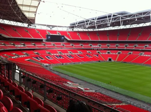 Interior view of Wembley Stadium, featuring red seating and a green pitch, with the word WEMBLEY displayed prominently.