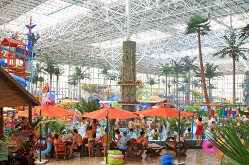 Indoor water park with slides, palm trees, and orange umbrellas. People are enjoying the pool area and attractions.