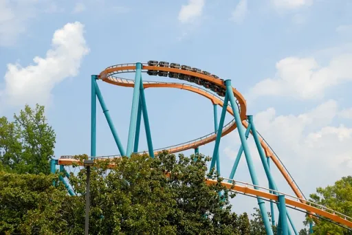 Roller coaster with orange and blue tracks loops against a cloudy sky.