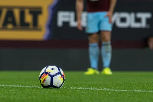 A football on the grass pitch with a blurred figure in the background.